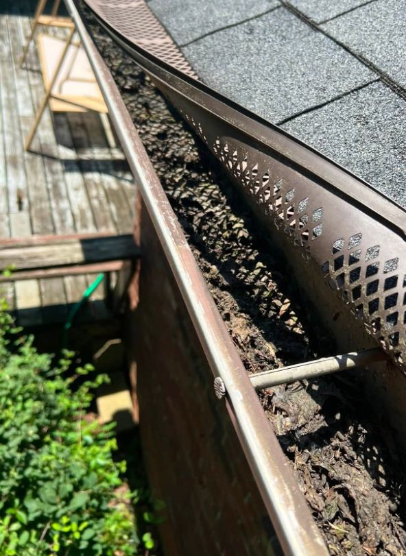 Perforated gutter guard with rotted debris packed in the gutter below it, gutter cleaning in Libertyville, IL