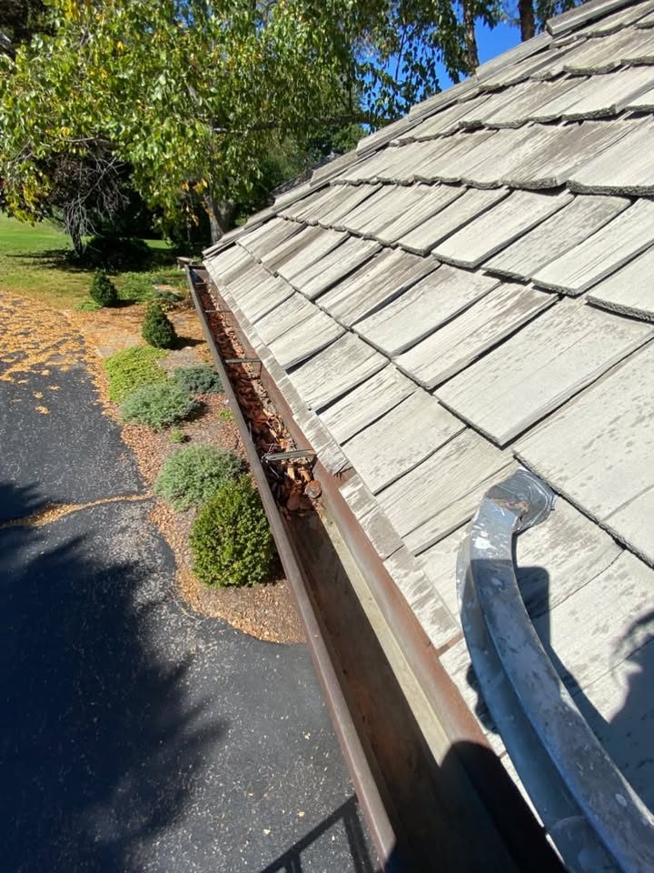 Gutter run packed with dry leaves along a cedar shake roof above a driveway, gutter cleaning in Libertyville, IL